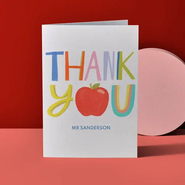 Personalised teacher thank you card with colourful lettering, apple illustration, and teacher name displayed on a red background.
